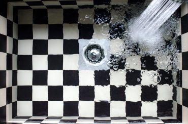 A shower head pouring water into a black and white checkered bathtub Description automatically generated